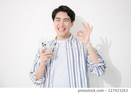 一位穿著襯衫的男士看著鏡頭，微笑著，用智慧型手機擺出「OK」或「好的」姿勢 127423263