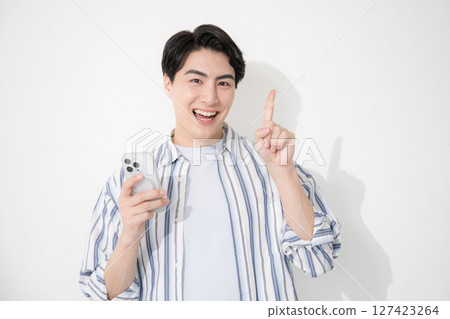 一名身穿襯衫的男子看著鏡頭，指著他的智慧型手機 127423264