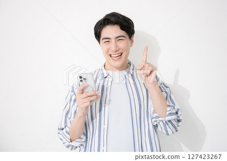 一名身穿襯衫的男子看著鏡頭，指著他的智慧型手機 127423267