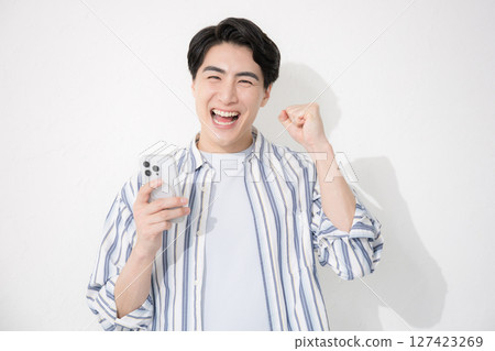 A man wearing a shirt looks at the camera, makes a fist pump with a smartphone and is motivated 127423269