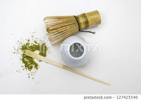 Traditional bamboo brush whisk with a spoon and matcha green tea powder splattered on white background. Accessories for making matcha green tea. Top view 127425540