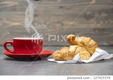 Croissants and cup of coffee on the table with wooden background 127425579