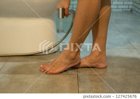 A woman's hand is spraying water to clean her feet. 127425676