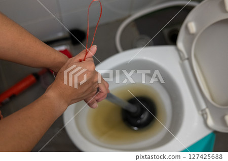 A woman's hand is using an air pump to solve a clogged toilet. 127425688