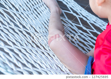 Asian boy sitting on a net with wound dressing plaster. 127425695