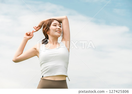 A woman in yoga wear stretching under the blue sky (exercise, deep breathing, sunbathing, refreshing, relieving stress) A woman in yoga wear stretching under the blue sky (exercise, deep breathing, sunbathing, refreshing, relieving stress) 127425806