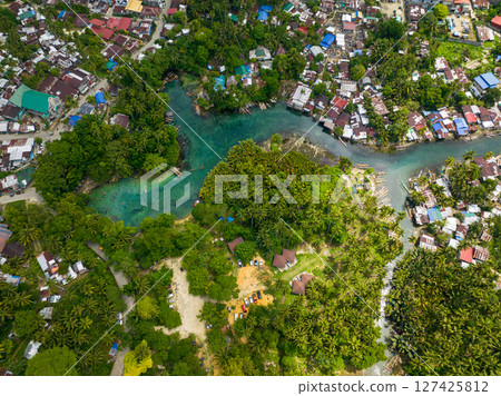Tropical forest and clear water in cold spring. Fishermans houses and boat. Bogac Cold Spring. Surigao del Sur, Philippines. Tropical forest and clear water in cold spring. Fishermans houses and boat. Bogac Cold Spring. Surigao del Sur, Philippines. 127425812
