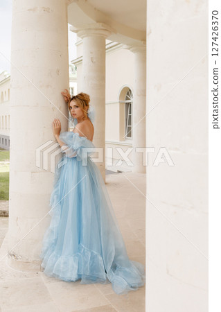 Elegant woman in blue ball gown posing near white stone column Elegant woman in blue ball gown posing near white stone column 127426370