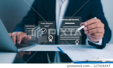 license agreement, Businessman uses a stylus to interact with documents, featuring digital checkmarks and signatures. Symbolizes efficient online contract management and modern legal agreements. 127426447