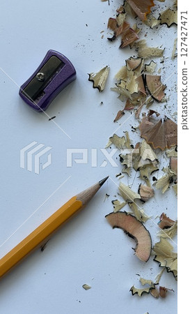 Yellow sharpened pencil with purple sharpener and wood shavings on white background. Concept of creativity, drawing and school supplies. Close-up top view. 127427471