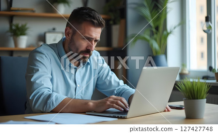 Focused middle aged man working on laptop in modern office space, surrounded by plants and natural light Focused middle aged man working on laptop in modern office space, surrounded by plants and natural light 127427748