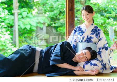 A man in a yukata relaxes on a woman's lap, smiling, enjoying a peaceful moment on the veranda in summer. A man in a yukata relaxes on a woman's lap, smiling, enjoying a peaceful moment on the veranda in summer. 127427871