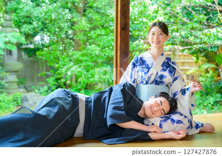 夏日的陽台場景，一名男子舒服地靠在身穿浴衣的女子腿上，女子慈祥地看著他。 127427876