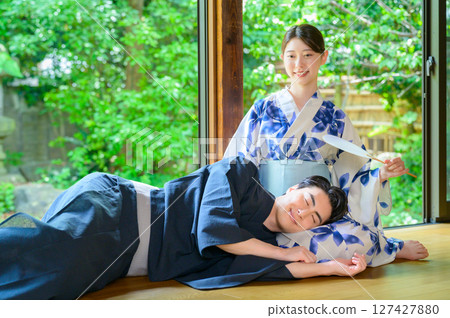 A peaceful everyday summer scene of a man and woman smiling in yukatas enjoying a knee pillow on the veranda 127427880