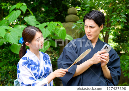 A summer scene in which a woman in a yukata tries to peer at a man using his smartphone, but the man shows signs of discomfort 127427898
