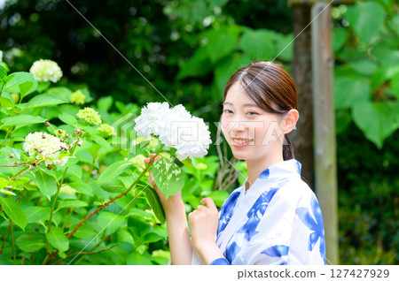 一幅清新自然的肖像畫，描繪了一位身著浴衣的女子在夏日花園中，一邊欣賞繡球花一邊優雅地微笑 127427929