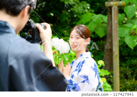 A photoshoot in which a man holding a camera and a woman in a yukata looking directly at him share a peaceful moment in natural light. 127427941