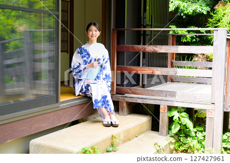 一位身著浴衣的女子坐在日式旅館的陽台上,手拿扇子,享受夏日的寧靜時光 一位身著浴衣的女子坐在日式旅館的陽台上,手拿扇子,享受夏日的寧靜時光 127427961