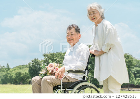 Elderly couple walking in wheelchairs in the park, a man in a wheelchair receiving a bouquet of flowers (seniors, men and women) 127428513