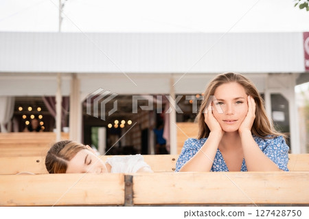Women Outdoor Cafe Worried: Two women display concern while seated outdoors at a cafe. 127428750