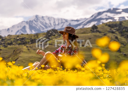 Woman Flowers Mountains: Brunette sits among yellow flowers, relaxed on mountain meadow, during daylight. Woman Flowers Mountains: Brunette sits among yellow flowers, relaxed on mountain meadow, during daylight. 127428835