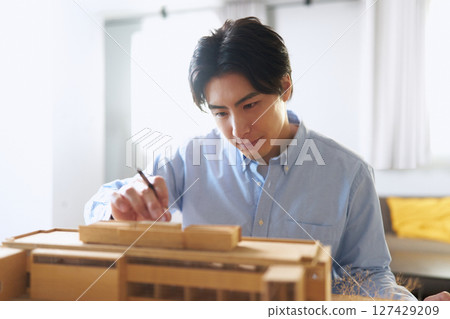 一位男建築師在辦公室看著一棟建築的模型,討論設計 一位男建築師在辦公室看著一棟建築的模型,討論設計 127429209