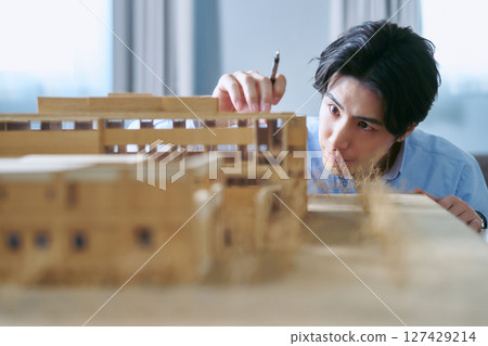 A man working on a building design looking at an architectural model in an office A man working on a building design looking at an architectural model in an office 127429214