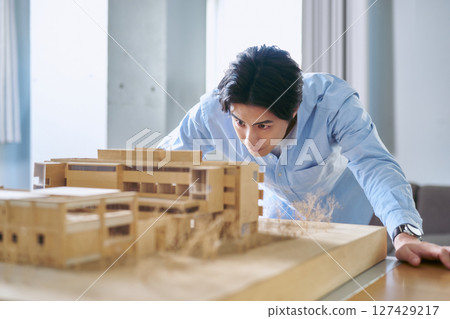一名男子正在查看建築模型,分析建築條件和預算,並製定計劃 一名男子正在查看建築模型,分析建築條件和預算,並製定計劃 127429217