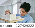 A male college student studying architecture designing a house by making a model of a building 127429222