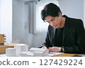 A male architect working in a design office checking architectural blueprints by looking at a building model and blueprints 127429224
