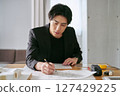 A male interior designer designs the interior of a house while checking the building blueprints 127429225