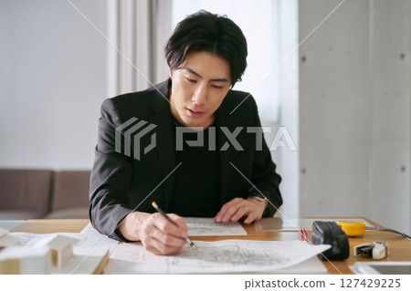 A male interior designer designs the interior of a house while checking the building blueprints 127429225