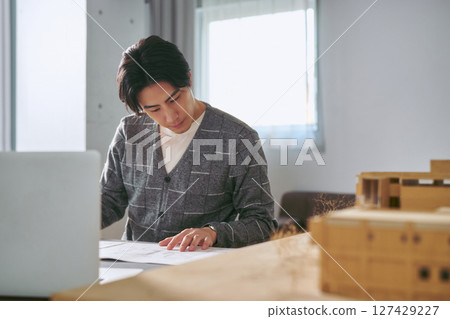A male architect working seriously in front of models and drawings in an architectural design office A male architect working seriously in front of models and drawings in an architectural design office 127429227