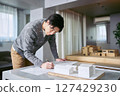 A male architect working on a design while checking and drawing blueprints at a desk with an architectural model 127429230