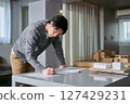 A male architect working at an atelier-style design office stands at a desk with a model of a building and writes plans 127429231