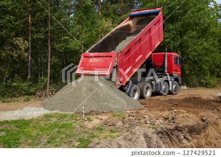 A dump truck tilts to pour gravel onto the ground at a construction site 127429521