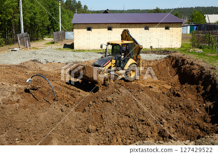A digger operates in a rural setting, carefully digging a deep excavation for the construction of a house.  127429522