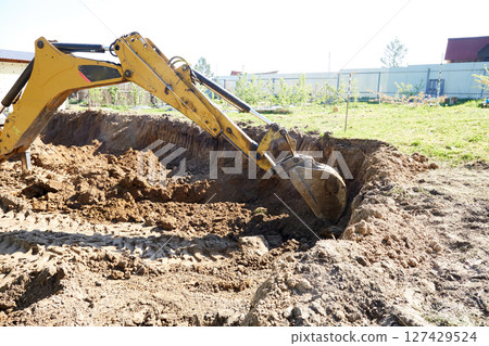 An excavator works in rural areas, carefully digging a deep excavation for the construction of a house. An excavator works in rural areas, carefully digging a deep excavation for the construction of a house. 127429524