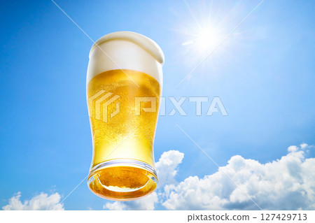 冰鎮啤酒泡沫從玻璃杯中溢出,背景是夏日藍天和陽光 冰鎮啤酒泡沫從玻璃杯中溢出,背景是夏日藍天和陽光 127429713