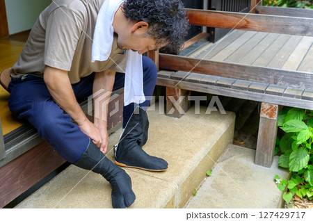 一名男子在早晨準備上班，在陽台上調整他的足袋襪。 127429717