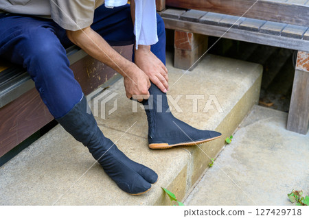 A moment before work begins, showing the careful attention to detail of the man checking that the black tabi socks fit his feet. A moment before work begins, showing the careful attention to detail of the man checking that the black tabi socks fit his feet. 127429718