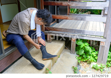 A typical Japanese scene of a man on a summer morning, taking his tabi socks and getting ready for work on the veranda. 127429719
