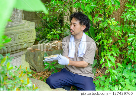 一個安靜的夏日早晨，一名男子準備上班，凝視著長滿青苔的燈籠，雙手握著工具。 127429760