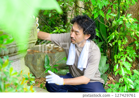 這是花園維護的場景，一名戴著白手套的男子輕輕地用手撫摸石燈籠，檢查是否有苔蘚和污垢。 127429761