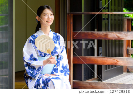 A woman in a yukata sits on the veranda of a wooden building and smiles while showing her fan, a tasteful everyday summer scene A woman in a yukata sits on the veranda of a wooden building and smiles while showing her fan, a tasteful everyday summer scene 127429818