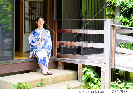 A woman in a yukata sitting on the stone steps of the veranda smiles as she spends a quiet and peaceful summer time at a ryokan. 127429821