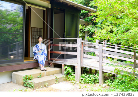 一位身著浴衣的女子坐在日式旅館的石階上,享受著被綠樹環繞的寧靜夏日時光。 一位身著浴衣的女子坐在日式旅館的石階上,享受著被綠樹環繞的寧靜夏日時光。 127429822