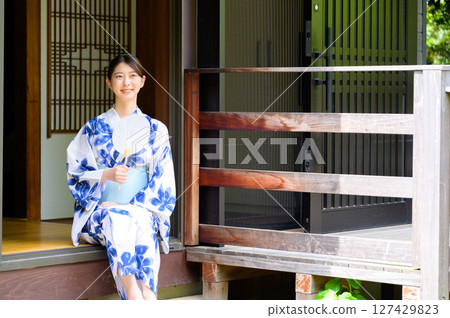 一位身著浴衣的女子坐在旅館的陽台上微笑，散發著夏日休閒和日式氛圍 127429823