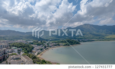June 7 2025 View of a Coastal Village with Statue Amidst Green Hills 127431777