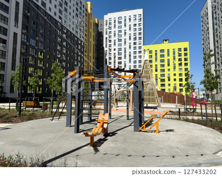 Outdoor fitness zone with professional street workout equipment surrounded by modern residential buildings, promoting active lifestyle, health and convenient daily exercise for all residents 127433202